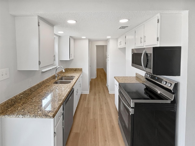 7620 Clover Ln, Watauga, TX 76148 - kitchen featuring stainless steel appliances, a sink, light wood-style floors, a textured ceiling, and light stone counters