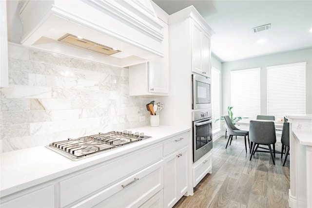 1507 Calcot Ln, Forney, TX 75126 - kitchen featuring stainless steel appliances, white cabinets, light countertops, tasteful backsplash, and premium range hood