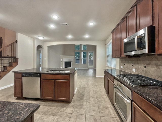 716 Setting Sun Trl, Mckinney, TX 75069 - kitchen with stainless steel appliances, arched walkways, tasteful backsplash, a kitchen island with sink, and dark stone countertops