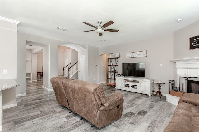 1253 Stone Ln, Celina, TX 75009 - living room featuring ceiling fan, arched walkways, light wood finished floors, a brick fireplace, and stairway