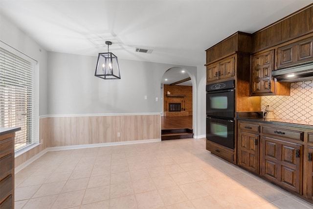7624 Lake Highlands Dr, Fort Worth, TX 76179 - kitchen featuring arched walkways, backsplash, under cabinet range hood, a wainscoted wall, and pendant lighting
