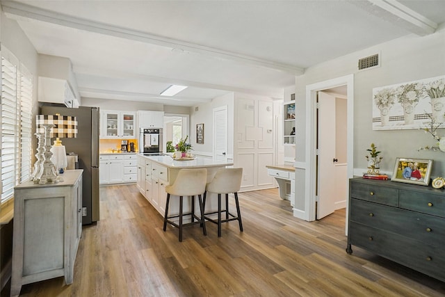 7208 Maranatha Ct, Colleyville, TX 76034 - kitchen featuring beam ceiling, appliances with stainless steel finishes, a kitchen breakfast bar, white cabinets, and wood finished floors