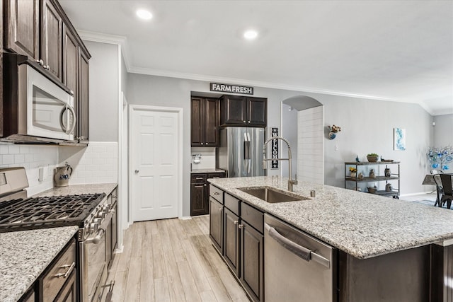 901 Freesia Dr, Little Elm, TX 75068 - kitchen featuring appliances with stainless steel finishes, a sink, crown molding, light wood-style floors, and arched walkways