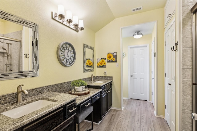 901 Freesia Dr, Little Elm, TX 75068 - bathroom with double vanity, wood finished floors, a tile shower, vaulted ceiling, and baseboards