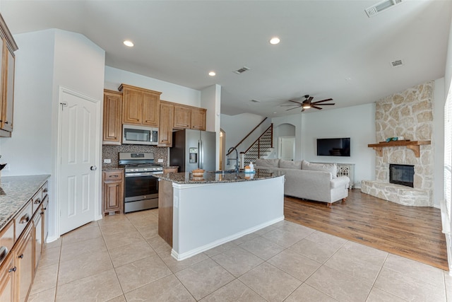 1012 Honeywell Dr, Anna, TX 75409 - kitchen with appliances with stainless steel finishes, light tile patterned flooring, dark stone counters, decorative backsplash, and a fireplace