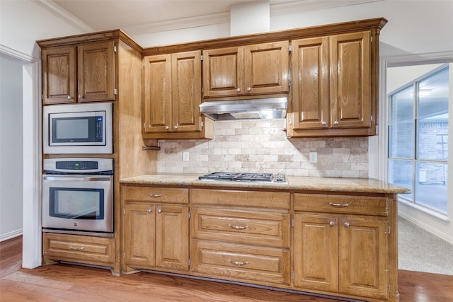 805 Evergreen Ct, Keller, TX 76248 - kitchen featuring appliances with stainless steel finishes, under cabinet range hood, decorative backsplash, ornamental molding, and light wood finished floors