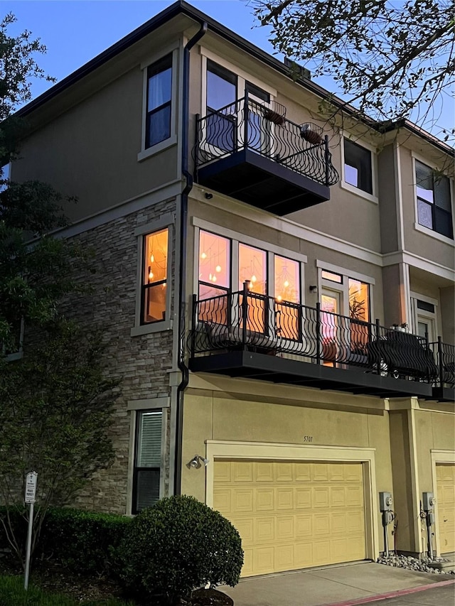 5701 Pantheon Ct, Plano, TX 75024 - rear view of house featuring a balcony, a garage, stucco siding, stone siding, and driveway