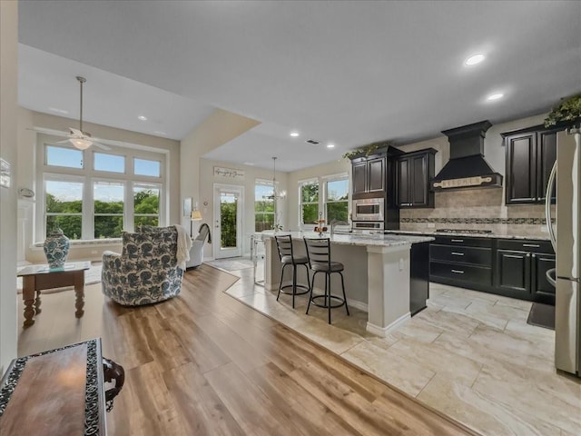 1316 Heather Ln, Little Elm, TX 75068 - kitchen featuring custom range hood, appliances with stainless steel finishes, a kitchen island with sink, a kitchen bar, and tasteful backsplash