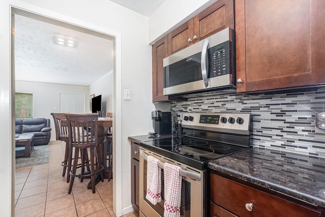4317 Hartford St Unit 102, Dallas, TX 75219 - kitchen featuring appliances with stainless steel finishes, decorative backsplash, light tile patterned floors, open floor plan, and a textured ceiling