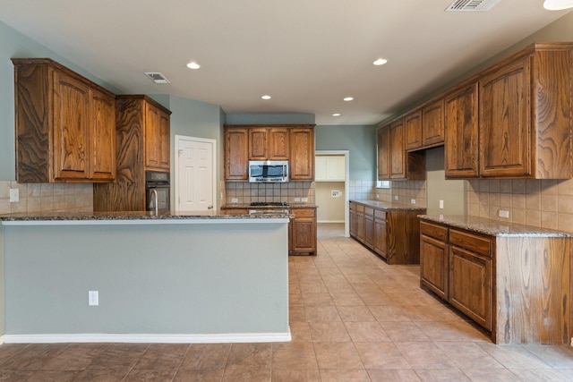 1908 Canyon Wren Dr, Mckinney, TX 75071 - kitchen with stainless steel microwave, dark stone countertops, a peninsula, decorative backsplash, and recessed lighting
