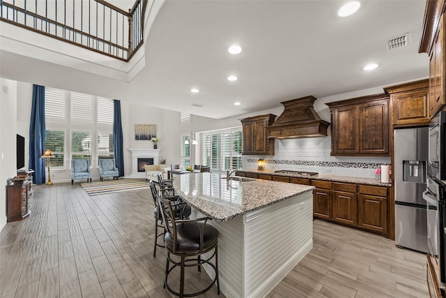 3300 Calvin Rd, Mckinney, TX 75071 - kitchen featuring custom range hood, a sink, light stone counters, a warm lit fireplace, and a high ceiling