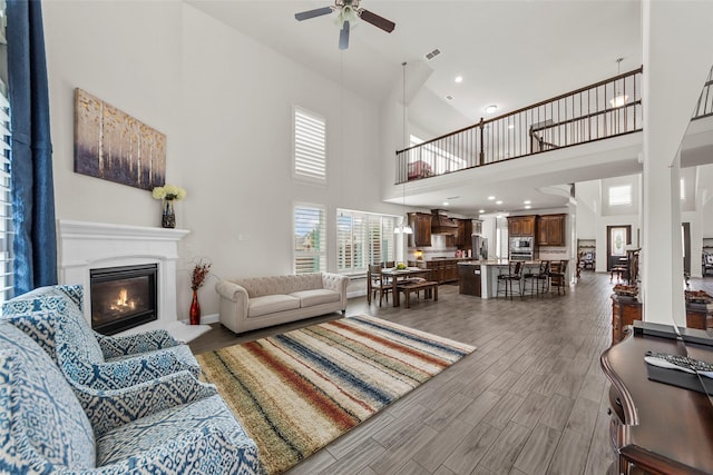 3300 Calvin Rd, Mckinney, TX 75071 - living room featuring ceiling fan, a towering ceiling, a glass covered fireplace, and wood finished floors