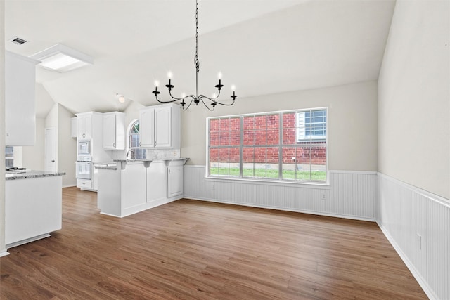 7816 Blossom Dr, Fort Worth, TX 76133 - kitchen with white oven, a wainscoted wall, wood finished floors, a chandelier, and white cabinetry