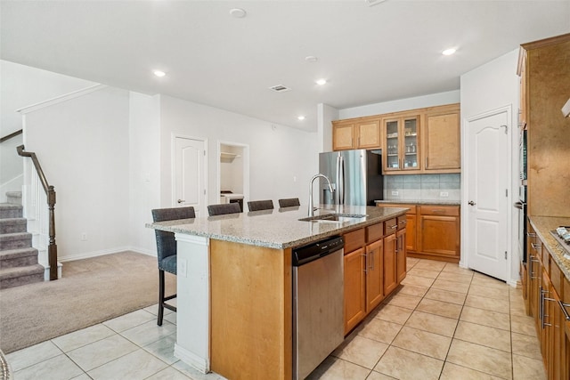 2612 Dancing Flame Dr, Denton, TX 76201 - kitchen featuring appliances with stainless steel finishes, light tile patterned floors, a breakfast bar area, light colored carpet, and an island with sink