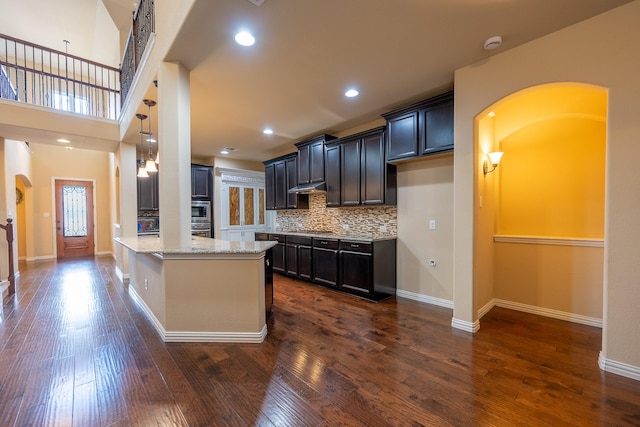 3548 Tuscan Hills Cir, Denton, TX 76210 - kitchen featuring arched walkways, under cabinet range hood, a peninsula, light stone counters, and dark wood-style flooring