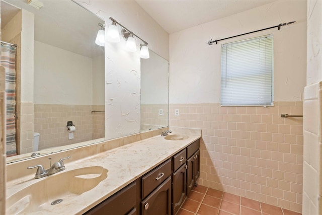 2801 Good Shepherd Dr, Brownwood, TX 76801 - full bath with tile walls, double vanity, tile patterned floors, toilet, and a wainscoted wall