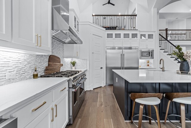 1733 Cousins Trl, Frisco, TX 75034 - kitchen featuring wall chimney exhaust hood, built in appliances, a kitchen breakfast bar, a sink, and white cabinetry