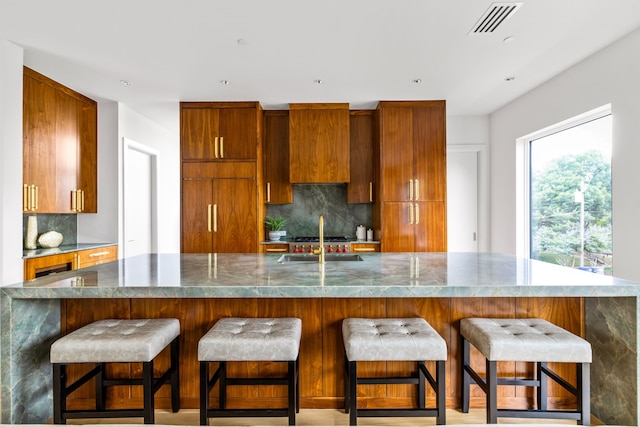 3909 Hawthorne Ave Unit 101, Dallas, TX 75219 - kitchen featuring a sink, tasteful backsplash, brown cabinets, a kitchen breakfast bar, and dark countertops