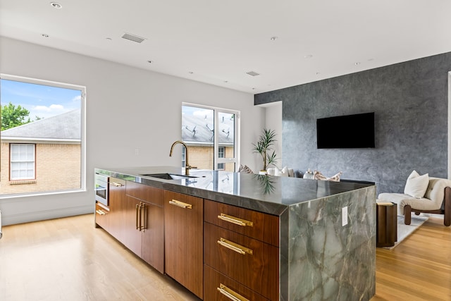 3909 Hawthorne Ave Unit 101, Dallas, TX 75219 - kitchen with a sink, light wood-style flooring, modern cabinets, a kitchen island with sink, and healthy amount of natural light