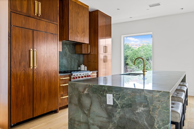 3909 Hawthorne Ave Unit 101, Dallas, TX 75219 - kitchen with a sink, a center island with sink, light wood finished floors, paneled built in fridge, and a breakfast bar area