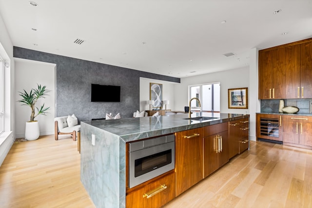 3909 Hawthorne Ave Unit 101, Dallas, TX 75219 - kitchen with wine cooler, stainless steel microwave, light wood-style flooring, a sink, and an island with sink