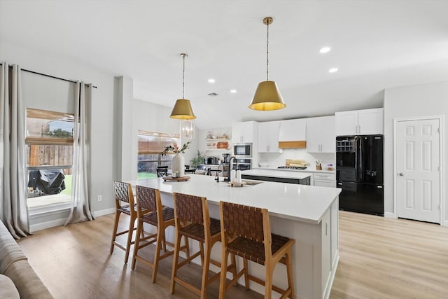 15429 Calico Ct, Frisco, TX 75035 - kitchen with freestanding refrigerator, stainless steel microwave, light wood-type flooring, light countertops, and a center island with sink