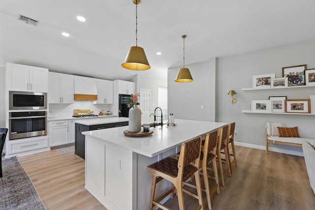 15429 Calico Ct, Frisco, TX 75035 - kitchen featuring appliances with stainless steel finishes, a center island with sink, light wood finished floors, white cabinets, and recessed lighting