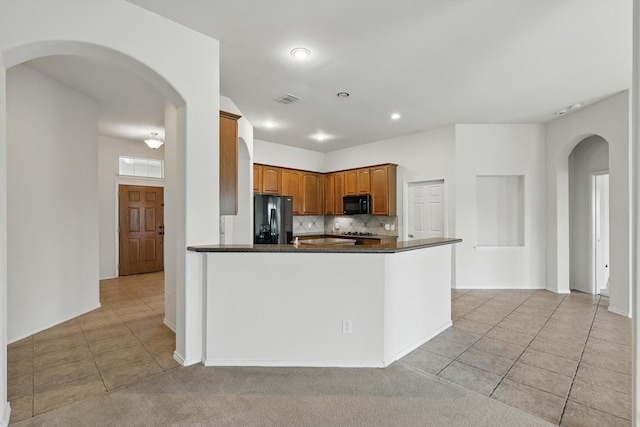 209 Lariat Dr, Fate, TX 75087 - kitchen featuring black appliances, light tile patterned flooring, arched walkways, backsplash, and brown cabinetry