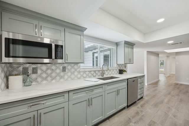 1629 Mesquite Trl, Plano, TX 75023 - kitchen with appliances with stainless steel finishes, gray cabinets, a sink, decorative backsplash, and light wood-type flooring