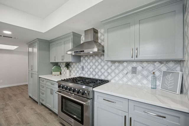 1629 Mesquite Trl, Plano, TX 75023 - kitchen with wall chimney range hood, stainless steel range, gray cabinetry, light wood-style floors, and light stone counters
