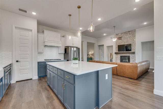 1302 Middleton Dr, Rockwall, TX 75087 - kitchen featuring freestanding refrigerator, custom exhaust hood, a brick fireplace, a ceiling fan, and white cabinetry