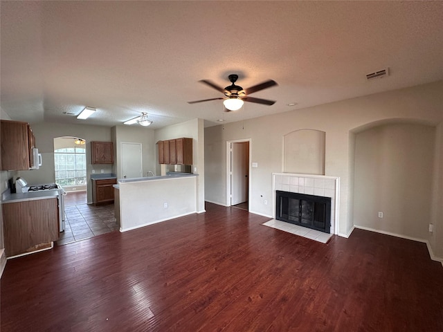 4102 Baccarat Dr, Garland, TX 75043 - unfurnished living room with a ceiling fan, dark wood-type flooring, a tile fireplace, arched walkways, and a textured ceiling