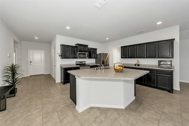 16608 Portage St, Justin, TX 76247 - kitchen featuring stainless steel appliances, a center island with sink, light countertops, dark cabinetry, and recessed lighting