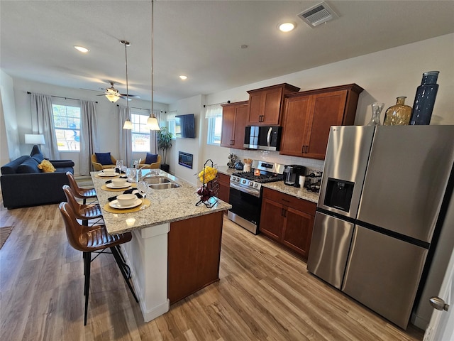 1836 Summer Aura, Mesquite, TX 75181 - kitchen featuring appliances with stainless steel finishes, a sink, a breakfast bar area, light wood-style floors, and open floor plan