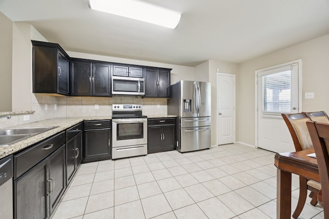 1035 Sadie St, Forney, TX 75126 - kitchen with appliances with stainless steel finishes, a sink, decorative backsplash, light tile patterned floors, and light stone countertops