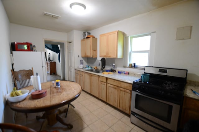 4413 Merida Ave, Fort Worth, TX 76115 - kitchen featuring stainless steel gas range oven, a sink, light countertops, freestanding refrigerator, and light brown cabinets