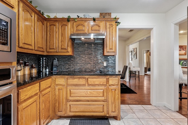 300 Burtonwood Cir, Ovilla, TX 75154 - kitchen with under cabinet range hood, appliances with stainless steel finishes, tasteful backsplash, light tile patterned flooring, and brown cabinetry