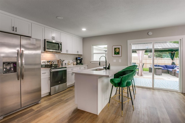 2110 Montana Trl, Grand Prairie, TX 76001 - kitchen featuring stainless steel appliances, a sink, light wood finished floors, backsplash, and a kitchen breakfast bar
