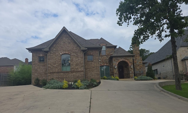 6801 Woodland Hills Dr, North Richland Hills, TX 76182 - french country home featuring brick siding, curved driveway, and a shingled roof