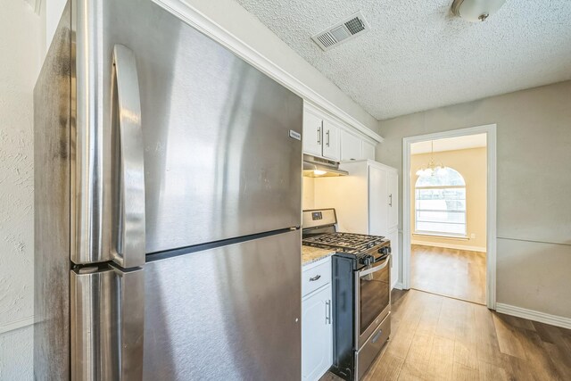 715 San Juan Dr, Duncanville, TX 75116 - kitchen with appliances with stainless steel finishes, under cabinet range hood, wood finished floors, a textured ceiling, and white cabinets
