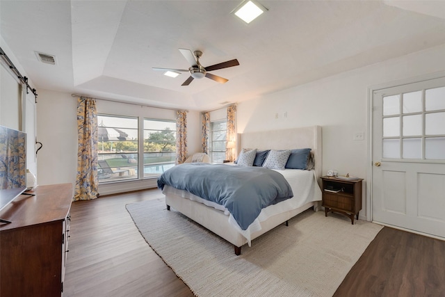8608 Funtier Ct, Fort Worth, TX 76179 - bedroom with light wood finished floors, a barn door, a tray ceiling, and a ceiling fan