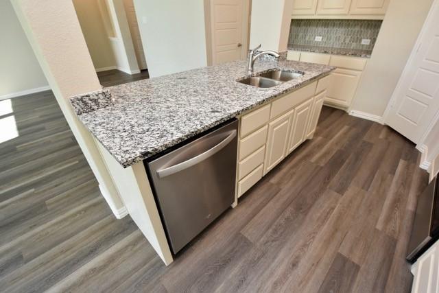 2408 Donella Dr, Denton, TX 76207 - kitchen with a sink, stainless steel dishwasher, light stone countertops, dark wood finished floors, and backsplash