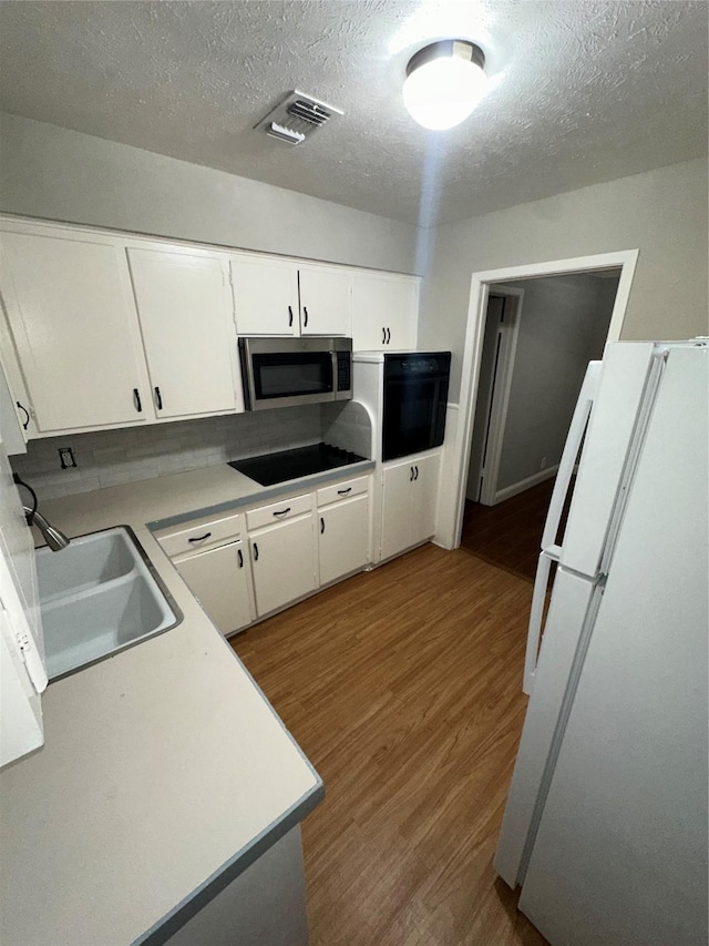 1303 N Morris St, Mckinney, TX 75069 - kitchen featuring black appliances, a sink, wood finished floors, a textured ceiling, and white cabinets