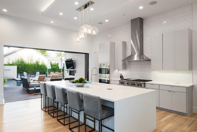 6420 Azalea Ln, Dallas, TX 75230 - kitchen with wall chimney exhaust hood, stainless steel appliances, a towering ceiling, modern cabinets, and a kitchen bar
