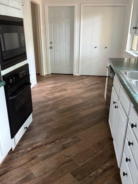 kitchen with black appliances, white cabinets, dark wood finished floors, and dark countertops