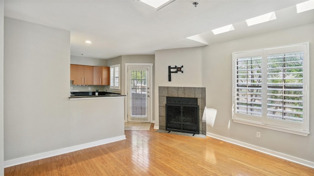 3901 Travis St Unit 230, Dallas, TX 75204 - unfurnished living room with baseboards, a skylight, light wood-type flooring, a fireplace, and recessed lighting