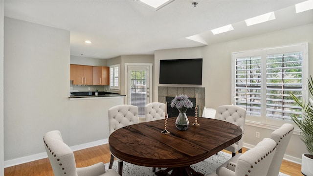 3901 Travis St Unit 230, Dallas, TX 75204 - dining area featuring a skylight, a tiled fireplace, baseboards, light wood-type flooring, and recessed lighting
