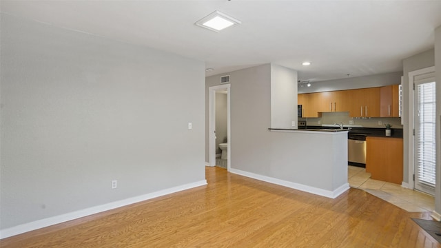 3901 Travis St Unit 230, Dallas, TX 75204 - kitchen featuring dark countertops, dishwasher, light wood-style floors, baseboards, and a sink