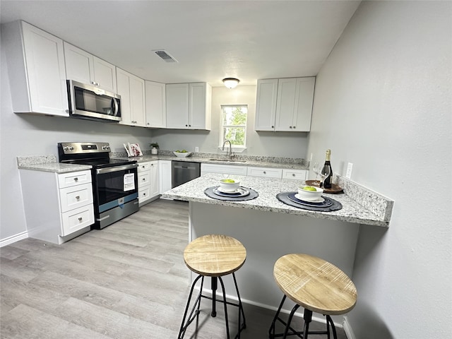 3801 Old Troup Hwy, Tyler, TX 75707 - kitchen with stainless steel appliances, a peninsula, a kitchen breakfast bar, white cabinetry, and light stone counters