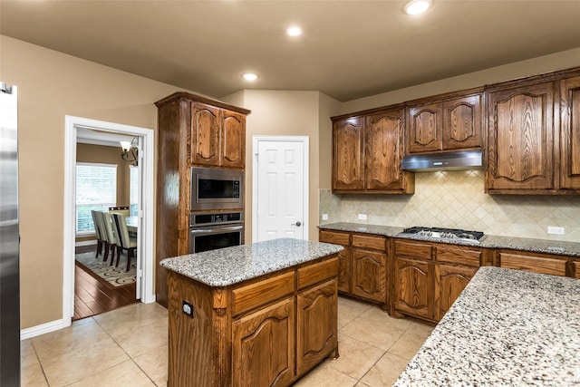 1518 E Oates Rd, Garland, TX 75043 - kitchen with appliances with stainless steel finishes, under cabinet range hood, a kitchen island, decorative backsplash, and light stone counters